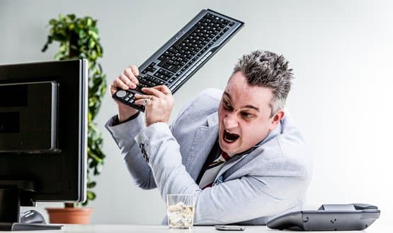 An angry man striking a computer with a keyboard