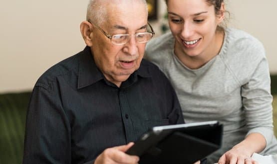 A young women teaches an older gentleman how to use a tablet computer