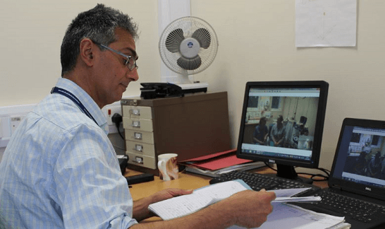 An NHS doctor consults with colleagues via video on his laptop
