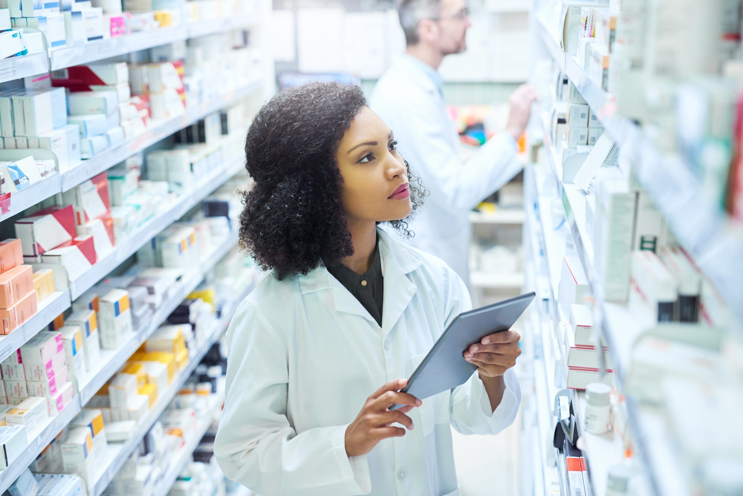 A young woman using a digital tablet to do inventory in a pharmacy.